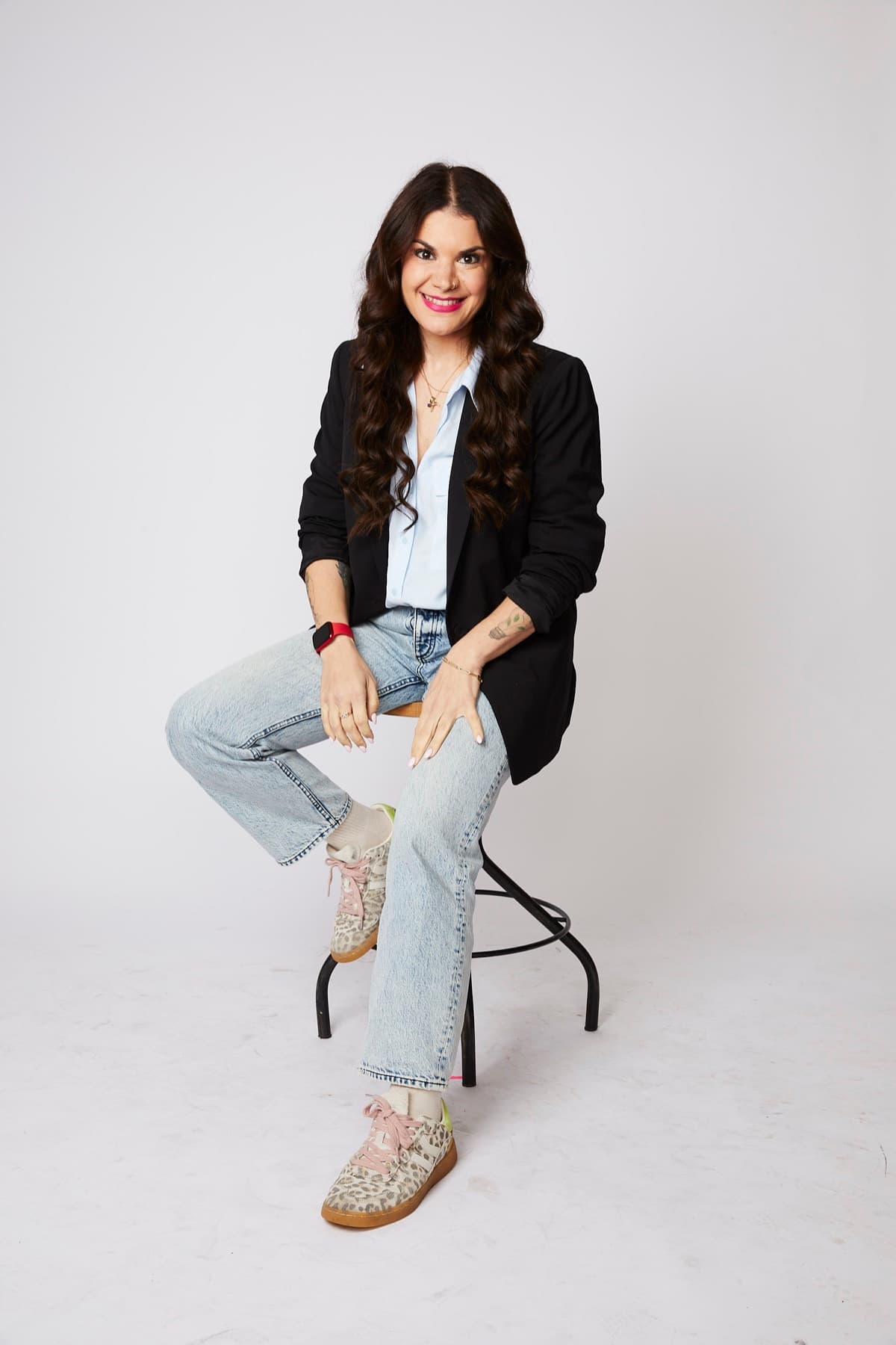 Vix Reitano, founder of Agency 6B, seated on a stool in a black blazer and light jeans, smiling at the camera